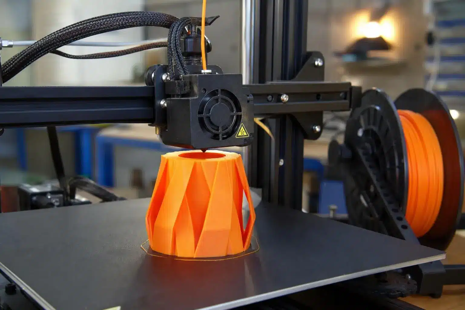 Impression 3D définition: pièce orange imprimée en forme géométrique complexe sur la plaque de construction d’une imprimante 3D.