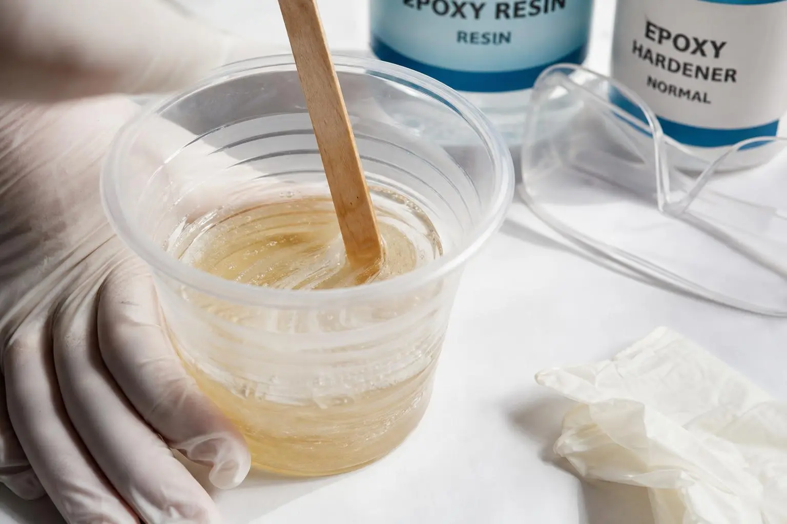 Préparation de résine époxy: mélange clair dans un gobelet avec bâtonnet, gants et bouteilles « epoxy resin » et « epoxy hardener » visibles. piéces techniques résine technique se sugèrent.